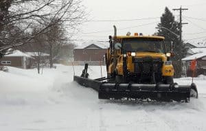 Snow removal with a yellow snowplow truck in a residential neighborhood during winter.